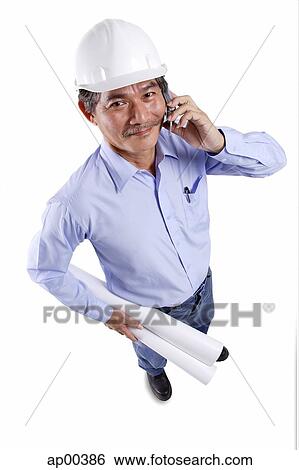 Mature man wearing construction hat, using mobile phone, carrying blueprints, looking at camera View Large Photo Image Stock Photograph - Mature man wearing construction hat, using mobile phone, carrying blueprints, looking at camera. Fotosearch