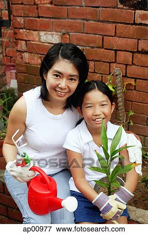 Mother and daughter, sitting in garden, holding plant and watering can View Large Photo Image Stock Photo - Mother and daughter, sitting in garden, holding plant and watering can. Fotosearch