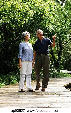 Senior couple standing in park, man pointing View Large Photo Image Stock Photo - Senior couple standing in park, man pointing. Fotosearch