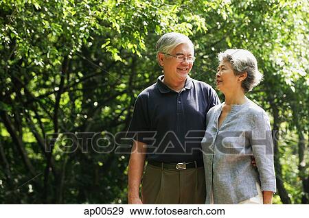Stock Photo - Senior couple standing in park, side by side, smiling. Fotosearch