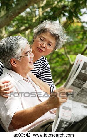 Stock Image - Senior man reading newspaper, woman behind him. Fotosearch