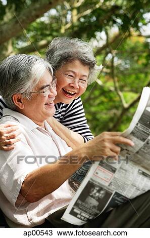 Senior man reading newspaper, woman embracing him from behind View Large Photo Image Stock Image - Senior man reading newspaper, woman embracing him from behind. Fotosearch