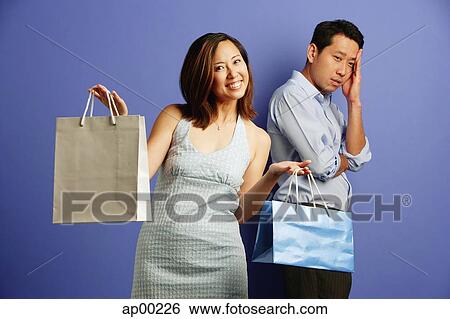 Stock Photograph - Smiling woman holding shopping bags, man behind her with hand on head. Fotosearch