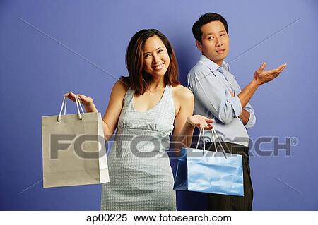 Stock Photography - Smiling woman holding shopping bags, sad man behind her with hand raised. Fotosearch