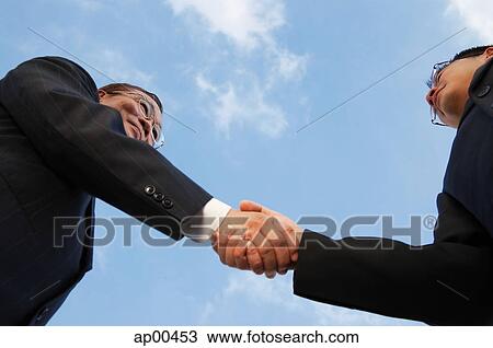 Stock Image - Two businessmen shaking hands, low angle view. Fotosearch