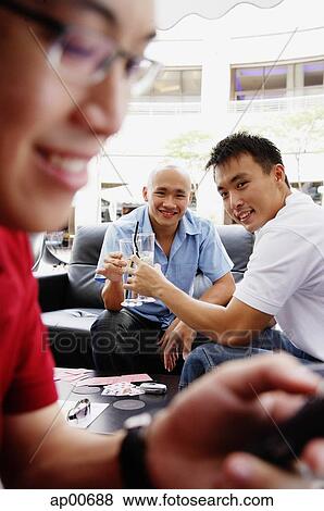 Two men toasting with drinks, looking at camera, another man using mobile phone in the foreground View Large Photo Image Stock Photo - Two men toasting with drinks, looking at camera, another man using mobile phone in the foreground. Fotosearch