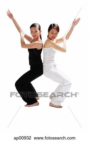 Stock Image - Two women back to back, bending knees, arms outstretched. Fotosearch