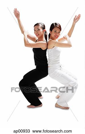 Stock Image - Two women back to back, bending knees, arms outstretched, smiling at camera. Fotosearch