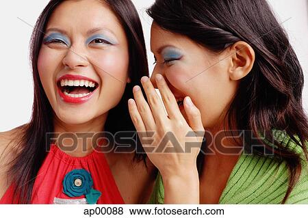 Stock Photo - Two women, one laughing, the other whispering in her ear. Fotosearch