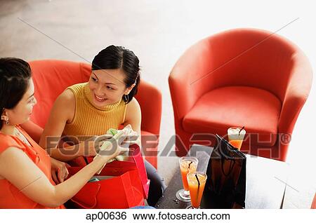 Stock Photograph - Two women sitting side by side, shopping bag between them. Fotosearch