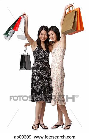 Two young women carrying shopping bags, smiling at camera View Large Photo Image Stock Photo - Two young women carrying shopping bags, smiling at camera. Fotosearch