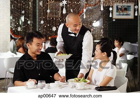 Stock Photo - Waiter serving couple at restaurant. Fotosearch