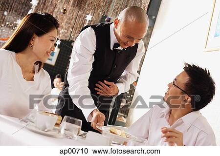 Stock Image - Waiter serving customers in restaurant. Fotosearch