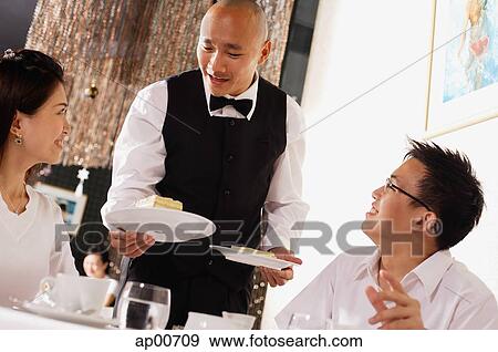 Stock Photo - Waiter serving plates of dessert to customers in restaurant. Fotosearch