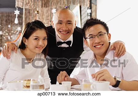 Stock Image - Waiter with couple at restaurant, looking at camera, smiling. Fotosearch