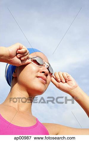 Stock Photo - Woman adjusting swimming goggles, looking away. Fotosearch