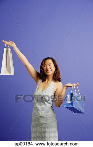 Woman against blue background carrying shopping bags, smiling View Large Photo Image Picture - Woman against blue background carrying shopping bags, smiling. Fotosearch