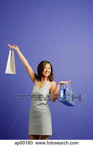 Stock Image - Woman against blue background carrying shopping bags. Fotosearch