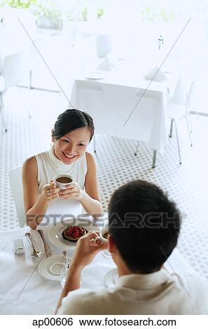 Stock Photograph - Woman and man at cafe, woman holding cup of coffee, high angle view. Fotosearch