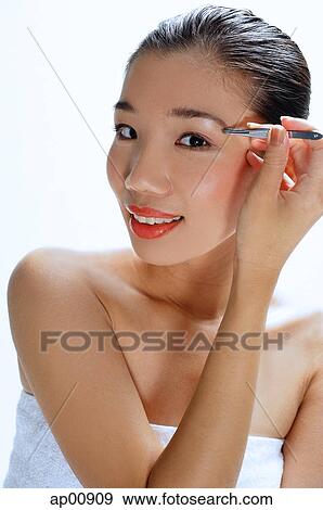 Stock Photo - Woman applying eye shadow, looking at camera. Fotosearch