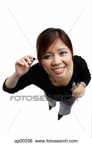 Stock Photograph - Woman applying mascara, looking up at camera. Fotosearch
