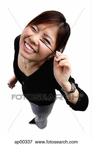 Stock Photo - Woman applying mascara, smiling at camera. Fotosearch