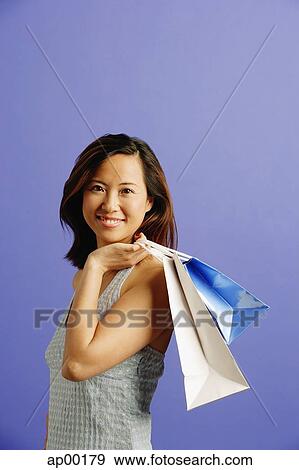 Stock Photo - Woman carrying shopping bags over shoulder, looking at camera. Fotosearch