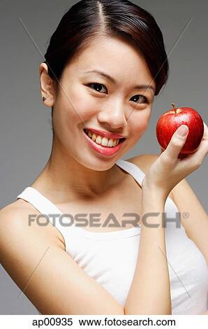 Stock Photography - Woman holding apple, looking at camera. Fotosearch