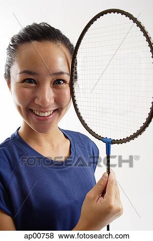 Stock Photo - Woman holding badminton racket next to her face, smiling. Fotosearch