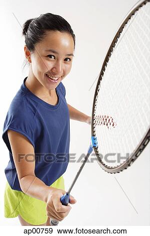 Stock Photo - Woman holding badminton racket, smiling up at camera. Fotosearch