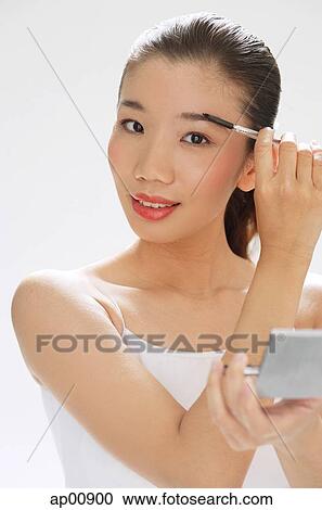 Stock Image - Woman holding brush to eyebrows, compact mirror on other hand. Fotosearch