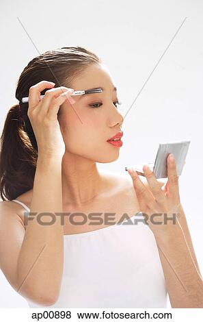 Stock Photo - Woman holding brush to eyebrows, looking at compact mirror. Fotosearch