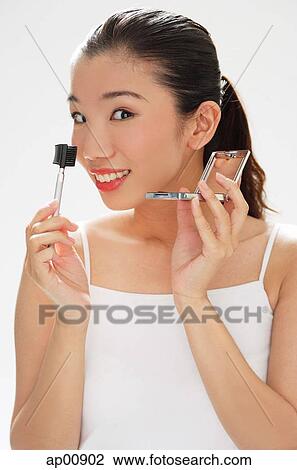 Stock Image - Woman holding eyebrow brush and compact, smiling at camera. Fotosearch