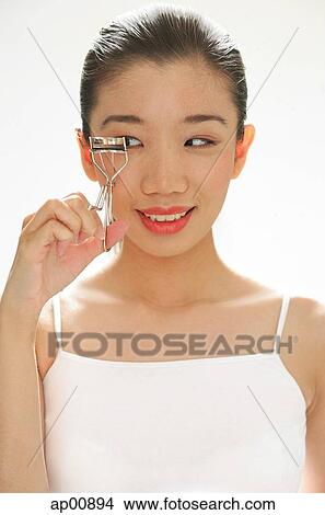 Picture - Woman holding eyelash curler, looking away. Fotosearch