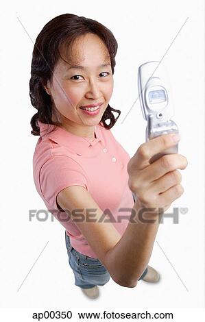 Stock Image - Woman holding mobile phone up, looking at camera. Fotosearch