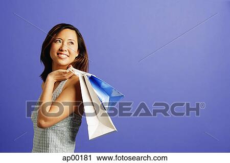 Stock Image - Woman holding shopping bags over shoulder, looking away. Fotosearch