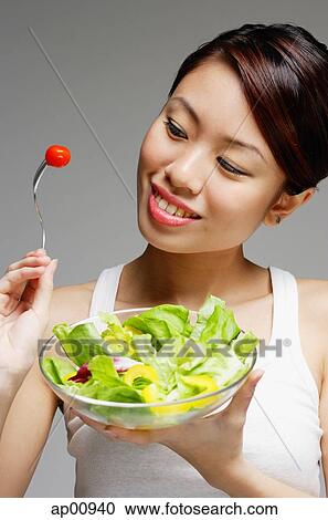 Woman looking at tomato on fork and holding bowl of salad View Large Photo Image Stock Image - Woman looking at tomato on fork and holding bowl of salad. Fotosearch