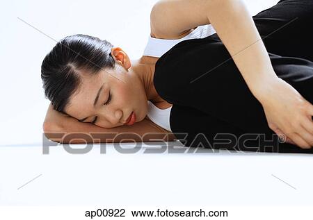 Stock Image - Woman lying on side, hugging knee, eyes closed. Fotosearch