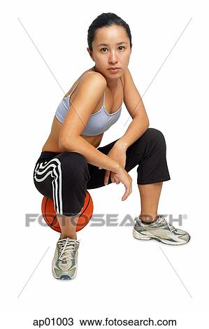 Stock Image - Woman sitting on basketball, looking at camera. Fotosearch