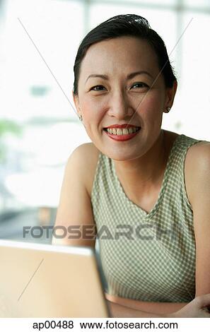 Stock Photo - Woman smiling at camera, laptop open in front of her. Fotosearch