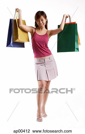 Stock Image - Woman standing, carrying shopping bags in both hands. Fotosearch