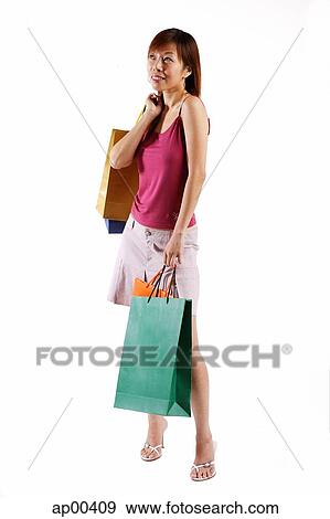 Stock Photo - Woman standing, carrying shopping bags, looking away. Fotosearch