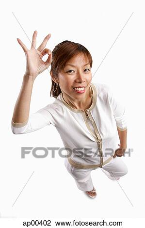 Stock Image - Woman standing, looking at camera, making hand sign. Fotosearch