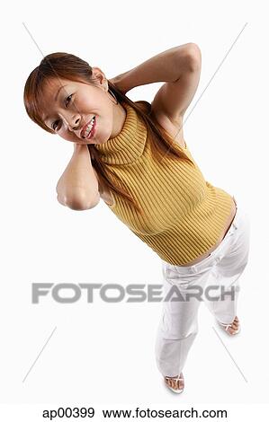 Stock Photo - Woman standing, looking at camera, hands behind head. Fotosearch