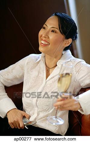 Stock Photo - Woman with champagne glass and mobile phone, looking away, smiling. Fotosearch