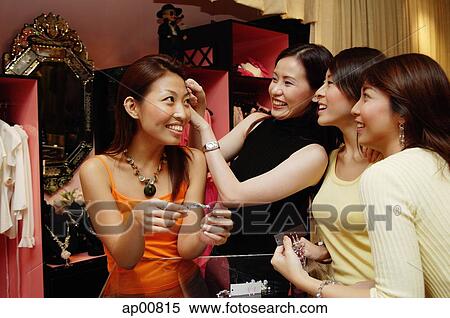 Stock Photography - Women at clothing store, one woman putting hair clip on another woman's head, others watching. Fotosearch