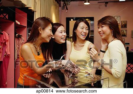 Picture - Women at clothing store, watching one woman try on earrings, smiling. Fotosearch
