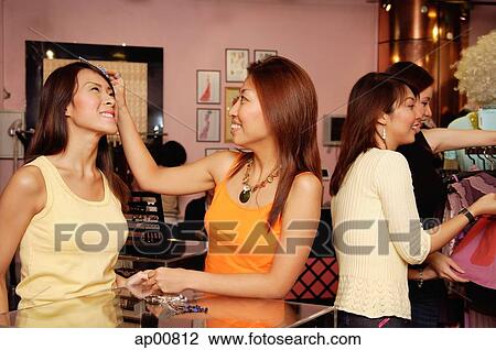 Stock Image - Women shopping, one woman adjusting her friend's hair. Fotosearch