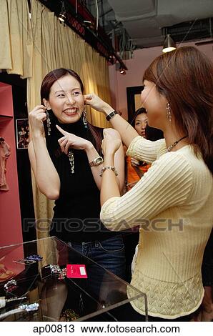 Stock Image - Women shopping, trying on earrings. Fotosearch