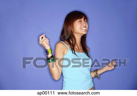 Stock Image - Young woman against blue background, snapping fingers. Fotosearch